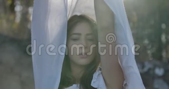 一个微笑的白种人女孩的特写镜头她站在阳光下举起一双浅白色的围巾视频的预览图