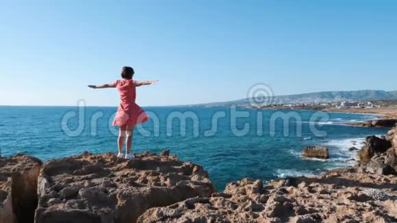 迷人的女孩站在悬崖边伸出手臂向两边穿红裙子的白种人女孩站在虚张声势视频的预览图