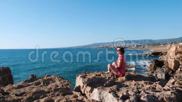 坐在悬崖上的女孩和太阳浴在太阳下的女孩的侧面景色年轻迷人的白种人女孩享受阳光看着大海布鲁纳视频的预览图