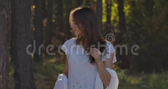 年轻神秘的高加索女人站在阳光下的森林里摸着她的头发浅白的漂亮姑娘视频的预览图