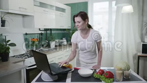 网上烹饪一个年轻漂亮的女孩站在旁边根据食谱视频准备新鲜蔬菜沙拉视频的预览图