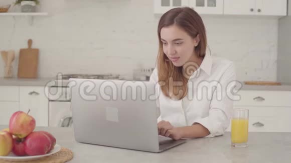 年轻的白人商人带着笔记本电脑坐在厨房做胜利的手势年轻漂亮的女孩视频的预览图