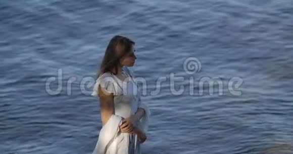 一位美丽的白种人女子站在海浪和思考的背景上穿着浅白的裙子视频的预览图