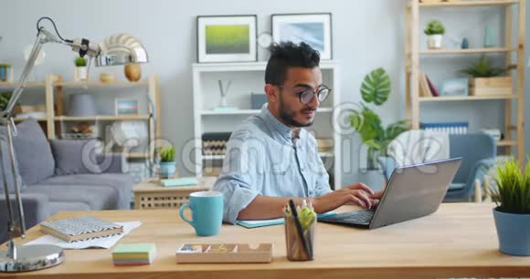 英俊的阿拉伯人用笔记本电脑工作然后在家里的办公桌上写笔记本视频的预览图