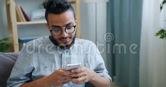 快乐的阿拉伯年轻人用智能手机看着屏幕带着快乐的脸回家视频的预览图