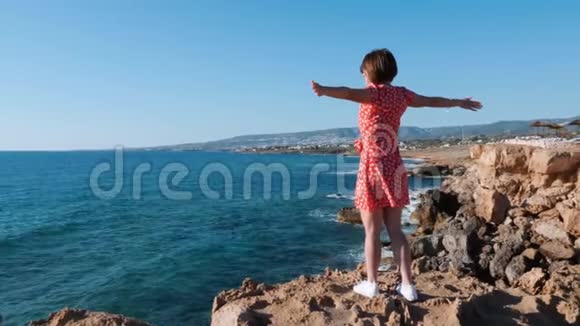 站在海边悬崖边的小女孩穿着红色衣服的白人女孩站在悬崖上看着大海女孩视频的预览图