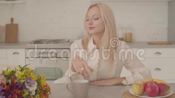 一位金发碧眼体贴入微的白种人女士端着一杯茶一杯咖啡和一束鲜花坐在桌旁视频的预览图