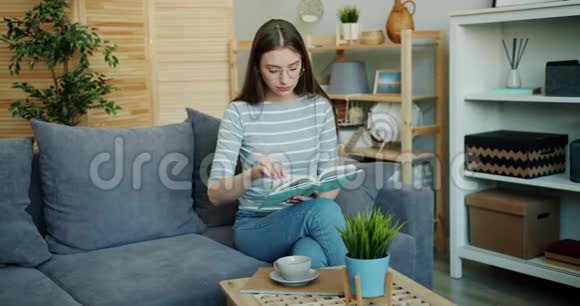 戴眼镜的聪明的年轻女士在平板沙发上坐着看书视频的预览图