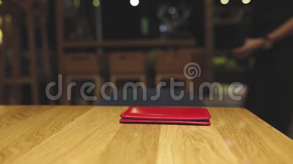 在咖啡馆或餐厅的棕色木桌上躺着红色皮革账单文件夹视频的预览图