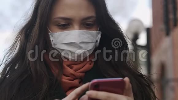 戴面罩的年轻女性在空街使用智能手机流行冠状病毒视频的预览图