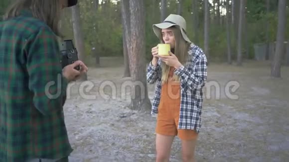 hipster一个人在一个小型的照相机上拍摄视频照片上摆着一个年轻漂亮的女孩背景是一杯茶或咖啡视频的预览图