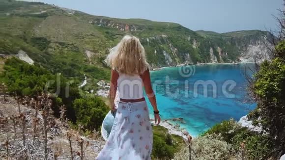 美丽的金发女人在希腊的凯法洛尼亚岛度假时举起双手戴太阳帽快乐生活夏日视频的预览图