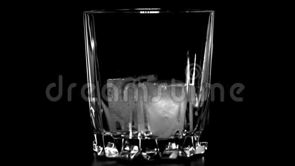 金色威士忌倒入玻璃将苏格兰威士忌或白兰地倒入带有黑色背景冰块的玻璃杯中视频的预览图