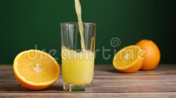 新鲜的黄色果汁被倒入一个高大的玻璃上的木制桌子橘子在绿色的背景视频的预览图