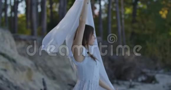 微笑的白种人女孩站在森林里举起手里拿着浅白色的围巾美丽的女人视频的预览图