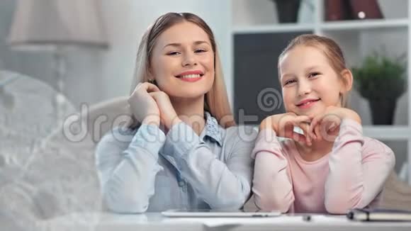 美丽的母亲和十几岁的女儿摆姿势微笑着看着相机在做家庭作业时放松视频的预览图