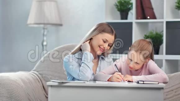 快乐的母亲帮助小学生的女儿做作业享受做母亲的乐趣视频的预览图