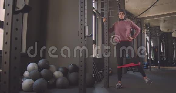 年轻漂亮的穆斯林女性戴头巾在室内健身房做腿部阻力训练的特写照片视频的预览图