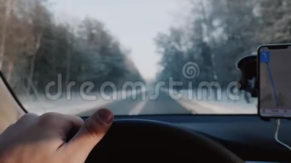 特写司机手握汽车方向盘在冬季道路上驾驶智能手机导航应用程序慢动作视频的预览图