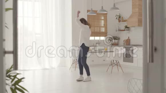 精力充沛的舞蹈一个快乐的白人女孩穿着休闲服装在轻盈的现代厨房快乐的美女视频的预览图
