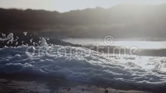 特写背景成堆厚厚的白色海泡沫摇晃着在狂风暴雨下飞离海滩慢动作视频的预览图