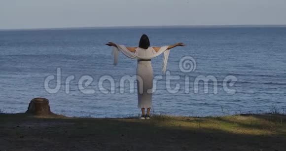 一位穿着浅色白裙的白种人女人站在波浪的背景上昂首阔步地站在后面视频的预览图