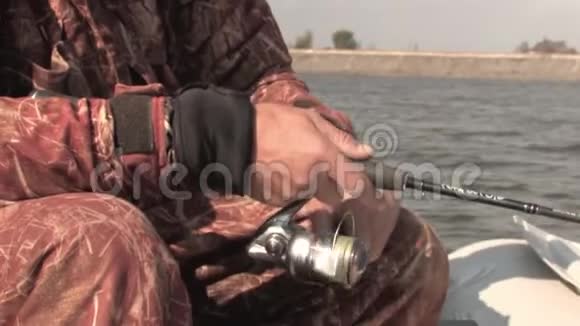 一个钓鱼的人坐在橡皮船上用一根纺棒钓鱼把鱼卷拧成一团把鱼线卷起来视频的预览图