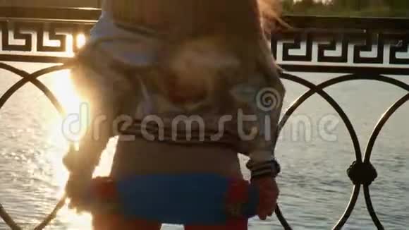 背着滑板的年轻女孩从背后摇着长发视频的预览图