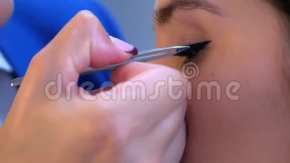 化妆师将人造睫毛涂抹在沙龙眼部特写的女孩模特身上视频的预览图