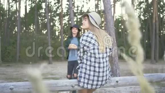 年轻的白种人女人坐在森林里穿着格子呢的时髦衬衫和帽子帅哥快到了视频的预览图