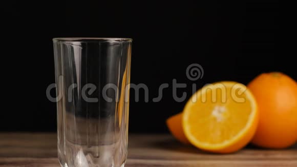 新鲜的黄色果汁倒在木桌上的一个高杯子里黑色背景上有橘子视频的预览图