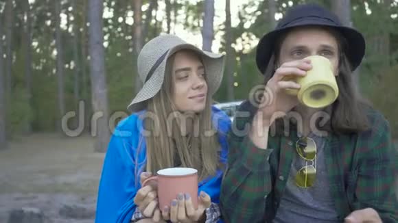 坐在森林里喝茶或咖啡的年轻夫妇快乐的白种人男女花时间视频的预览图