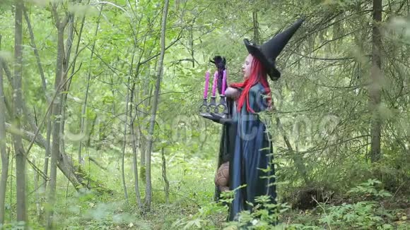 一个红头发黑帽子和一件外套的年轻女巫正在森林里施展魔法视频的预览图