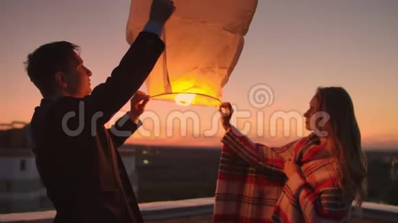 一个男人和一个女孩穿着格子布在屋顶上发射一盏天灯视频的预览图