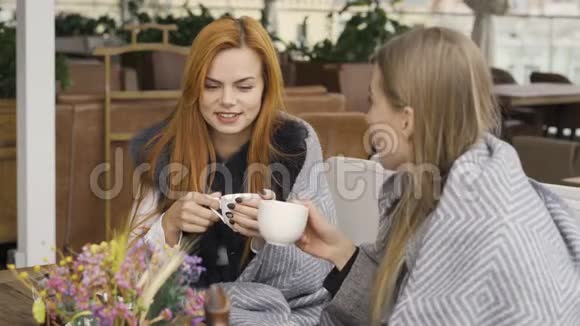 两个漂亮的白种人女朋友裹着毯子坐在咖啡馆里聊天喝热茶青年妇女视频的预览图