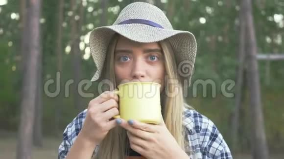 年轻快乐的白种人女孩穿着格子衬衫戴着帽子从黄色的杯子里喝着茶或咖啡微笑着和咖啡视频的预览图