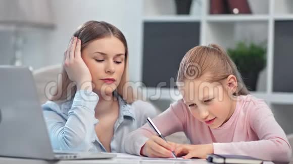 专注的母亲和微笑的小学生十几岁的女儿一起做学校作业中等特写视频的预览图