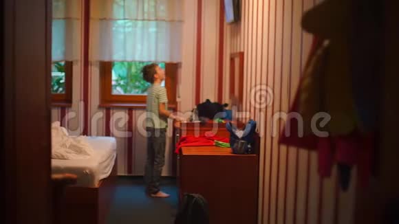 一个困倦的男孩一大早就站在酒店的电视附近视频的预览图