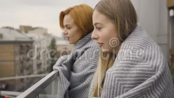 两个穿着毯子的白种人女朋友站在阳台上远远地看着两个女人在聊天视频的预览图