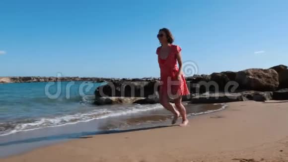 年轻的黑发女孩穿着红色短裙沿着海岸奔跑高加索辣妹在海上可爱的女孩在沙滩上奔跑视频的预览图