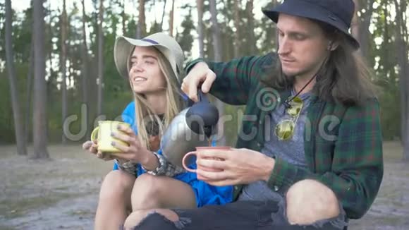一对年轻的白种人游客穿着格子衬衫和帽子把茶倒进杯子里男朋友和女朋友视频的预览图