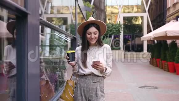 慢动作漂亮微笑的年轻女士戴着时尚的帽子站在办公楼附近有街咖啡厅使用视频的预览图
