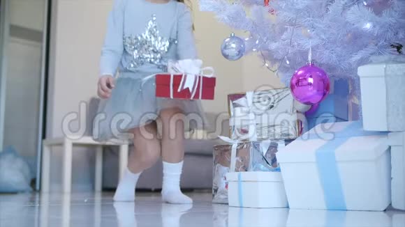 小天使女孩完美微笑的时间推移视频把一个红色的礼物盒和白色的蝴蝶结放在圣诞树下视频的预览图