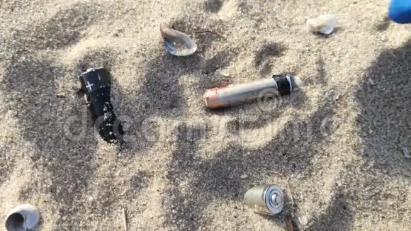 男人蓝手套手在海滩上收集有毒废物沙子里的锂离子电池环境污染的概念视频的预览图