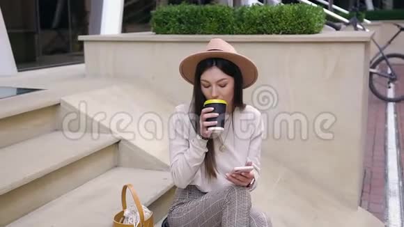 靠近迷人的梦幻年轻女士戴着时髦的帽子和时尚的衣服一边坐着一边享受新鲜咖啡视频的预览图