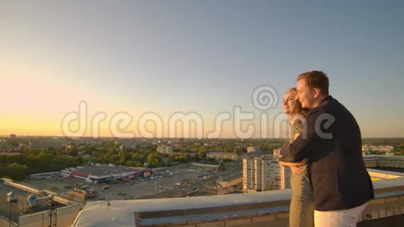 日落时分站在屋顶上的一男一女拥抱着看着美丽的景色视频的预览图
