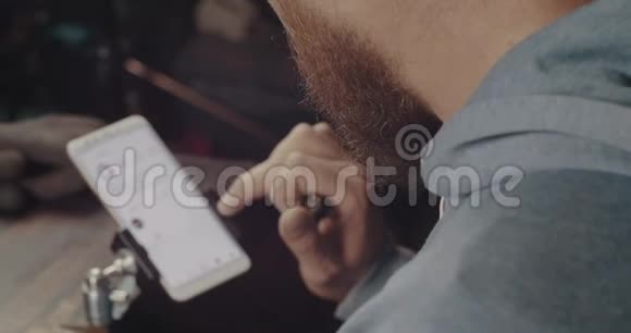 手机屏幕上放着红胡子的男人从上面看人类正在触摸智能手机的触摸屏电影院视频的预览图