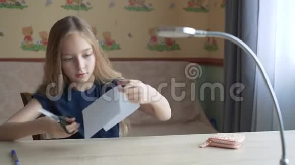 可爱专注的女孩坐在书桌和剪纸纸上视频的预览图