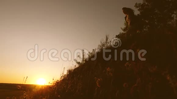 一个女旅行者向一个男人伸出手在夕阳下爬上山顶旅行者手牵着手爬上悬崖视频的预览图