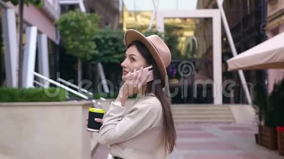 30岁的女人戴着时髦的帽子在美丽的现代建筑附近走来走去聊天视频的预览图